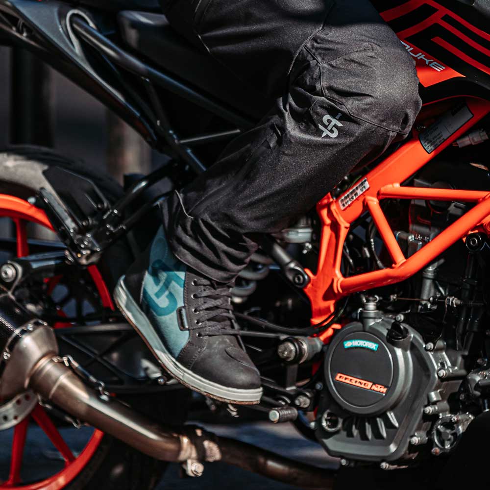 biker on motorbike riding wearing black and blue trainers with black waterproof trousers for men